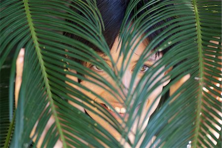 simsearch:633-06406668,k - Woman looking through palm leaves Stock Photo - Premium Royalty-Free, Code: 633-06406363