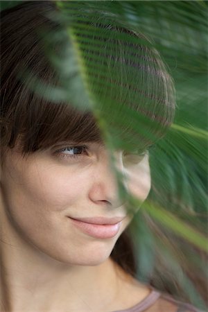 simsearch:633-06406668,k - Young woman behind palm frond, looking away in thought Stock Photo - Premium Royalty-Free, Code: 633-06406502