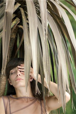 simsearch:633-06406668,k - Young woman behind tropical foliage, hand covering one eye Stock Photo - Premium Royalty-Free, Code: 633-06406503