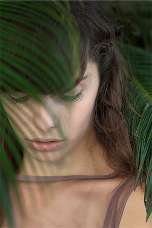 simsearch:633-06406668,k - Young woman behind palm frond, looking down sadly Stock Photo - Premium Royalty-Free, Code: 633-06406566