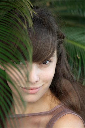 simsearch:633-06406668,k - Young woman behind palm frond, portrait Stock Photo - Premium Royalty-Free, Code: 633-06406678