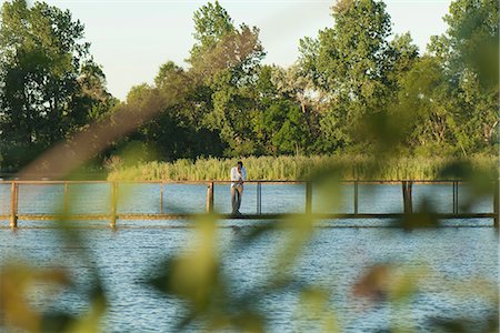 simsearch:633-01573604,k - Homme debout sur la passerelle sur la rivière à distance, vue travers les feuilles en avant-plan flou Photographie de stock - Premium Libres de Droits, Code: 633-06406743