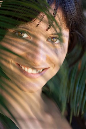 simsearch:633-06406668,k - Young woman looking through palm leaf, smiling, portrait Stock Photo - Premium Royalty-Free, Code: 633-06406779