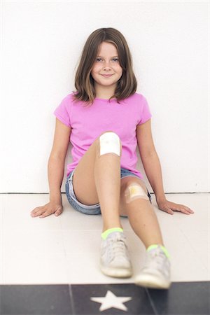 Girl sitting on floor with both knees bandaged, smiling Stock Photo - Premium Royalty-Free, Code: 633-08150951