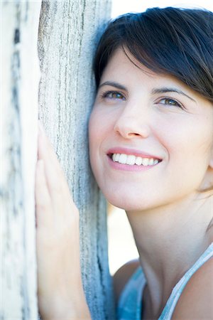 simsearch:696-03401960,k - Woman leaning against tree trunk, smiling cheerfully Stock Photo - Premium Royalty-Free, Code: 633-08482209