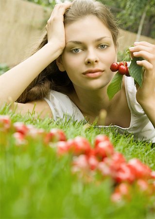 simsearch:633-01272776,k - Woman lying in grass holding up cherries, looking at camera Foto de stock - Royalty Free Premium, Número: 633-01274740