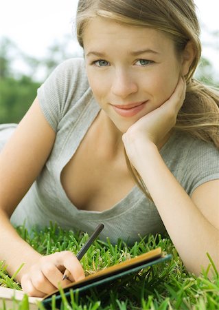 Young woman reclining in grass with notebook and pencil, portrait Stock Photo - Premium Royalty-Free, Code: 633-01273049