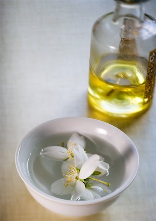 Mock orange flowers floating in bowl and bottle of massage oil Stock Photo - Premium Royalty-Free, Code: 633-01273172