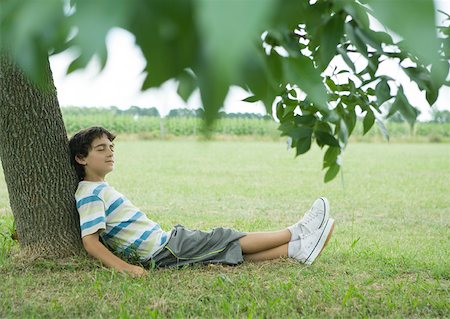 Boy sitting on ground, leaning against tree, eyes closed Stock Photo - Premium Royalty-Free, Code: 633-01273390