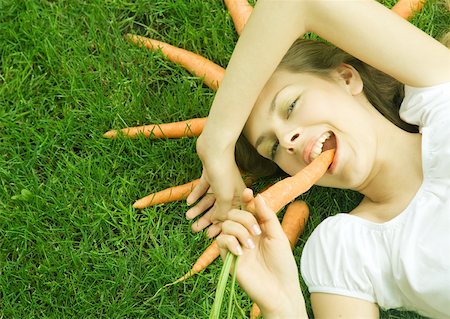 simsearch:633-01274090,k - Femme couchée sur l'herbe, manger des carottes, carottes disposées autour de la tête, souriant à la caméra Photographie de stock - Premium Libres de Droits, Code: 633-01273612