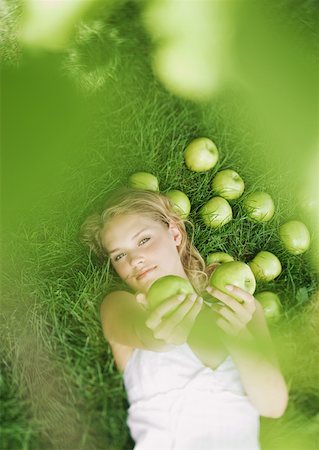 Woman lying in grass, holding up apples toward camera Stock Photo - Premium Royalty-Free, Code: 633-01273890