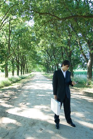 simsearch:633-01574593,k - Businessman standing in rural road, holding briefcase and cell phone Stock Photo - Premium Royalty-Free, Code: 633-01574295