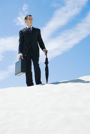 Businessman standing on dune, holding briefcase and umbrella, low angle view Stock Photo - Premium Royalty-Free, Code: 633-01574614