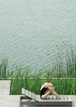 simsearch:633-01572866,k - Woman sitting on lounge chair next to lake, hugging knees, resting head on arms Stock Photo - Premium Royalty-Free, Code: 633-01572881