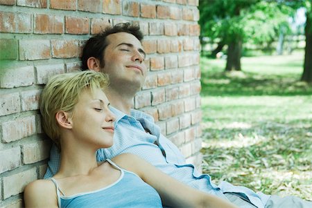 Couple sitting outdoors, leaning against brick wall, smiling, eyes closed Stock Photo - Premium Royalty-Free, Code: 633-01573108