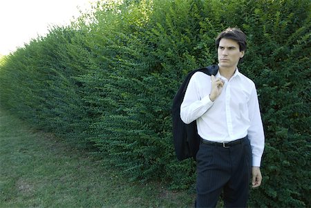 simsearch:633-01573622,k - Businessman standing by hedge, holding jacket over shoulder, looking away Foto de stock - Royalty Free Premium, Número: 633-01573537