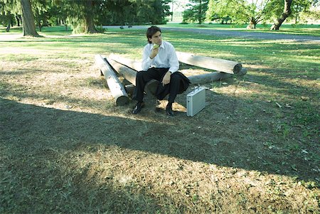 simsearch:633-01573622,k - Businessman sitting on logs, eating an apple, looking away Fotografie stock - Premium Royalty-Free, Codice: 633-01573549