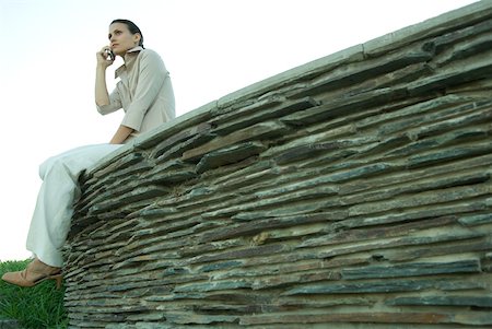 simsearch:633-01574322,k - Businesswoman sitting on stone wall, using cell phone, low angle view Stock Photo - Premium Royalty-Free, Code: 633-01573573