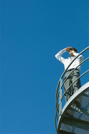 simsearch:633-01573622,k - Businessman standing on metal balcony, looking away, low angle view, blue sky in background Foto de stock - Royalty Free Premium, Número: 633-01573592