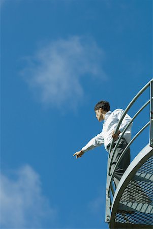 simsearch:633-01573606,k - Homme debout sur le balcon métallique, pointant à distance, vue d'angle faible, ciel bleu en arrière-plan Photographie de stock - Premium Libres de Droits, Code: 633-01573593