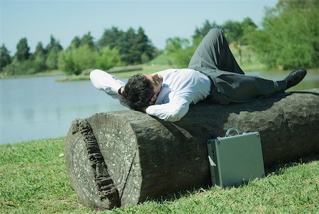 simsearch:633-01573622,k - Businessman lying on tree trunk, hands behind head Foto de stock - Royalty Free Premium, Número: 633-01573621