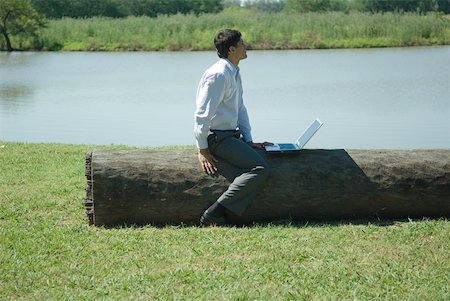 simsearch:633-01573622,k - Businessman sitting on tree trunk with laZSop, looking away Fotografie stock - Premium Royalty-Free, Codice: 633-01573622