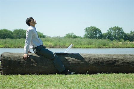 simsearch:633-01573622,k - Businessman sitting on tree trunk with laZSop, looking up Foto de stock - Royalty Free Premium, Número: 633-01573623