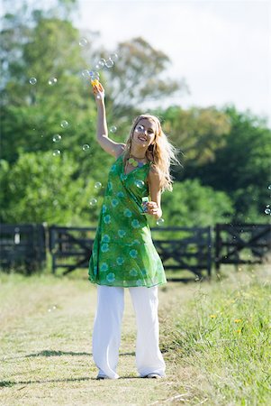 simsearch:633-01992711,k - Young woman blowing bubbles in rural field, smiling at camera Stock Photo - Premium Royalty-Free, Code: 633-01714095