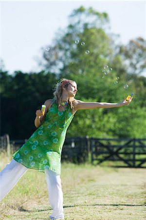 simsearch:633-05402126,k - Young woman blowing bubbles in rural field with arm outstretched, standing on one leg Stock Photo - Premium Royalty-Free, Code: 633-01714096