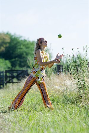 Young woman standing in field with legs apart, juggling apples Stock Photo - Premium Royalty-Free, Code: 633-01714099