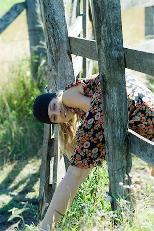 Young woman climbing through wooden fence, smiling at camera Stock Photo - Premium Royalty-Free, Code: 633-01714146