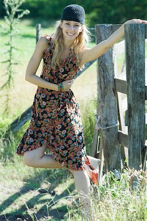 simsearch:633-01714195,k - Young woman standing on one leg and holding on to rural fence, smiling at camera Stock Photo - Premium Royalty-Free, Code: 633-01714147