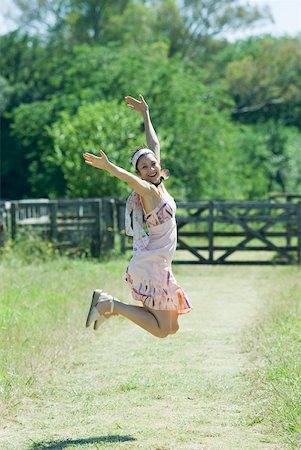 simsearch:633-01714195,k - Young woman jumping with arms raised in rural setting, smiling at camera Stock Photo - Premium Royalty-Free, Code: 633-01714194