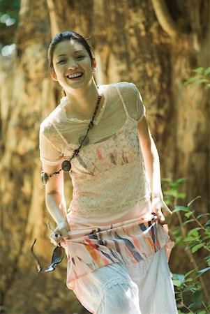 simsearch:633-01714195,k - Young woman walking in woods, holding up skirt, smiling at camera Stock Photo - Premium Royalty-Free, Code: 633-01714208