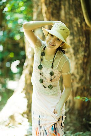 simsearch:633-01714195,k - Young woman standing in woods, holding sunhat on head, smiling at camera Stock Photo - Premium Royalty-Free, Code: 633-01714217