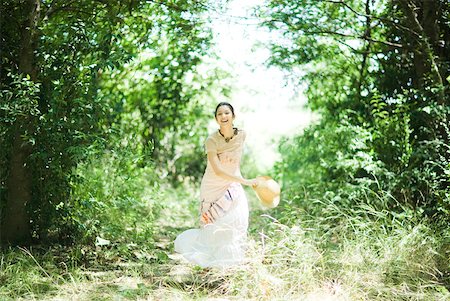 simsearch:633-01714195,k - Young woman running in woods, holding sunhat, smiling at camera Stock Photo - Premium Royalty-Free, Code: 633-01714224