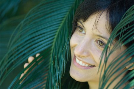 simsearch:633-02231736,k - Young woman among palm leaves, smiling, looking away, portrait Foto de stock - Sin royalties Premium, Código: 633-01714243