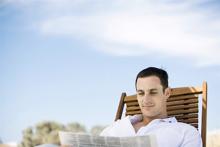 Young man sitting in deck chair, reading newspaper Stock Photo - Premium Royalty-Free, Code: 633-01714424