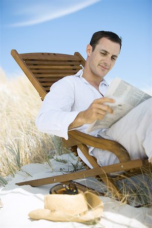 Young man sitting in deck chair on beach, reading newspaper Stock Photo - Premium Royalty-Free, Code: 633-01714427