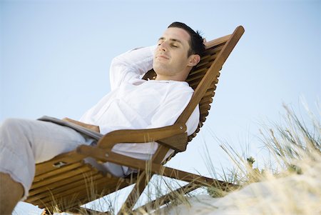 Young man sitting in deck chair, smiling, low angle view Stock Photo - Premium Royalty-Free, Code: 633-01714423