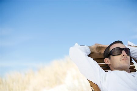 Young man sitting in deck chair, wearing sunglasses Stock Photo - Premium Royalty-Free, Code: 633-01714430