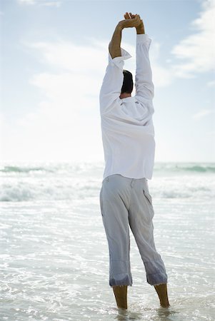 summer beach break - Young man standing in surf, stretching, rear view Stock Photo - Premium Royalty-Free, Code: 633-01714448