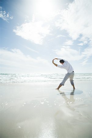 summer beach break - Young man standing in surf, stretching, rear view Stock Photo - Premium Royalty-Free, Code: 633-01714452