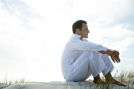 Young man sitting on dune, smiling, full length Stock Photo - Premium Royalty-Free, Code: 633-01714464