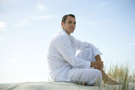 Young man sitting on dune, listening to earphones, smiling, looking away Stock Photo - Premium Royalty-Free, Code: 633-01714466