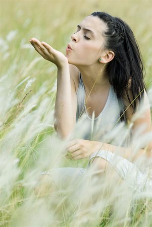 Teenage girl crouching in tall grass with eyes closed, blowing seedling Stock Photo - Premium Royalty-Free, Code: 633-01714603