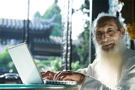 simsearch:696-03394943,k - Elderly man wearing traditional Chinese clothing using laZSop, smiling at camera Stock Photo - Premium Royalty-Free, Code: 633-01714708