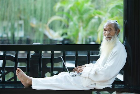 portrait chinese old man - Elderly man wearing traditional Chinese clothing, using laZSop, full length Stock Photo - Premium Royalty-Free, Code: 633-01714741