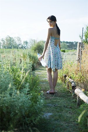 simsearch:633-01715082,k - Young woman standing in garden with bottle of water, looking over shoulder at camera Stock Photo - Premium Royalty-Free, Code: 633-01715073