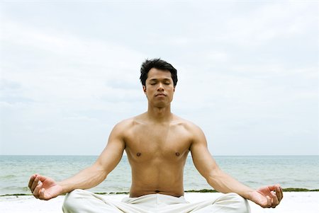 Barechested man sitting in lotus position, ocean in background Stock Photo - Premium Royalty-Free, Code: 633-01715166